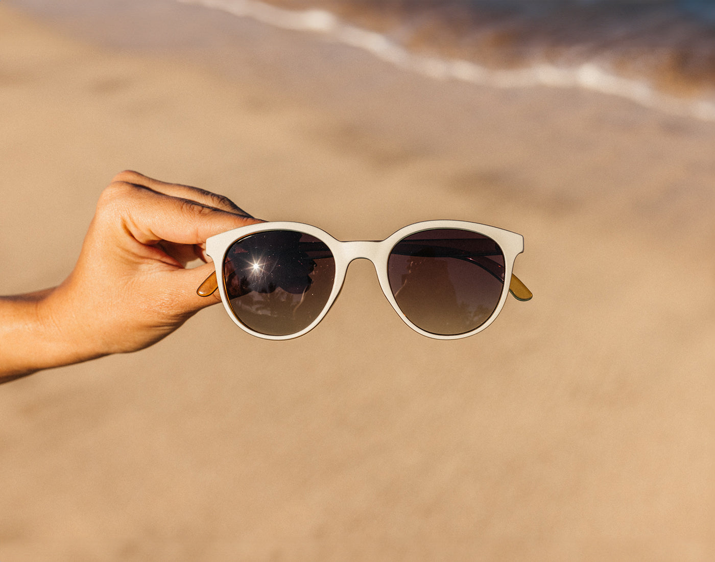 hand holding sunski makani sunglasses on beach