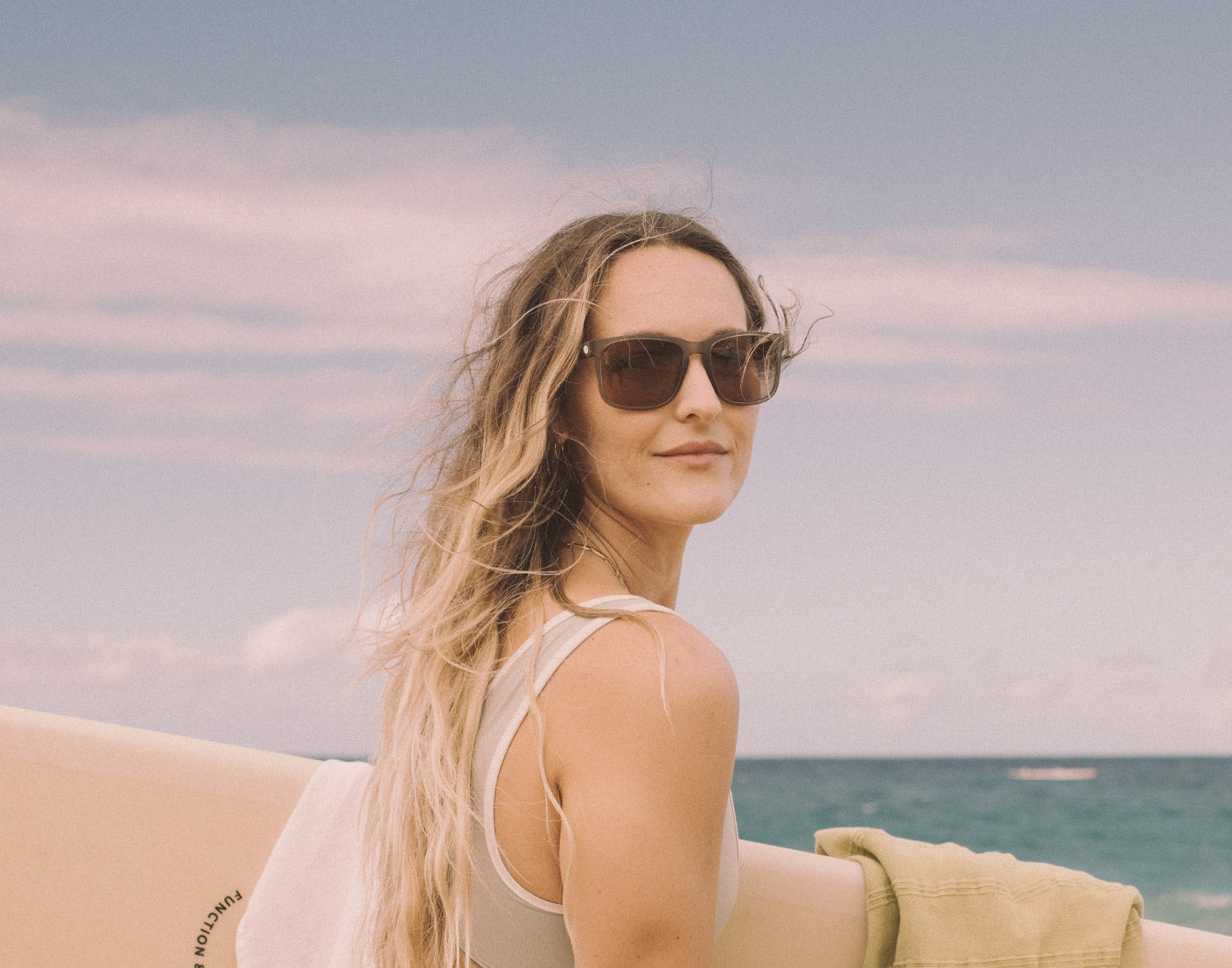 girl holding surfboard wearing sunski kiva sunglasses