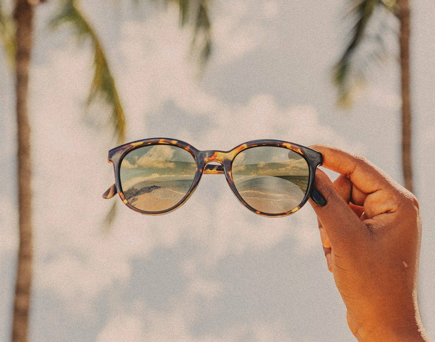 hand holding sunski makani flash gold sunglasses in the sky