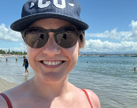 Person wearing a cap and sunglasses at a beach with water and sky in the background