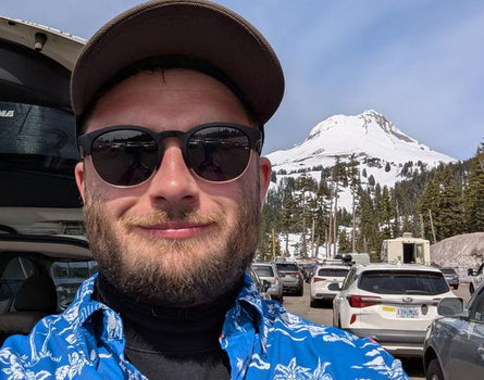 Man wearing sunglasses and a cap with a mountain and parking lot in the background