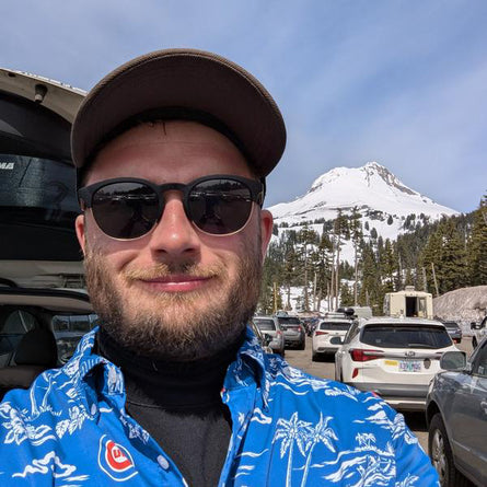 Man wearing sunglasses and a cap with a mountain and parking lot in the background
