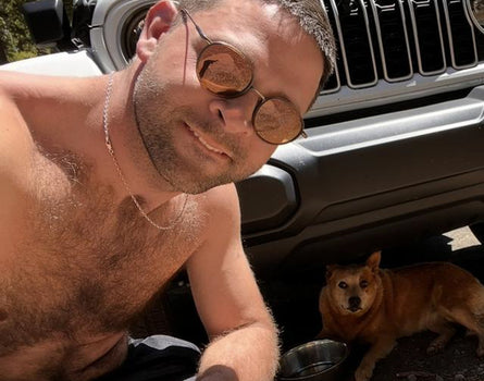 Man with sunglasses and a dog sitting next to a Jeep