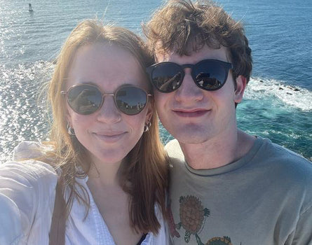 Two people taking a selfie by the ocean with sunglasses on.