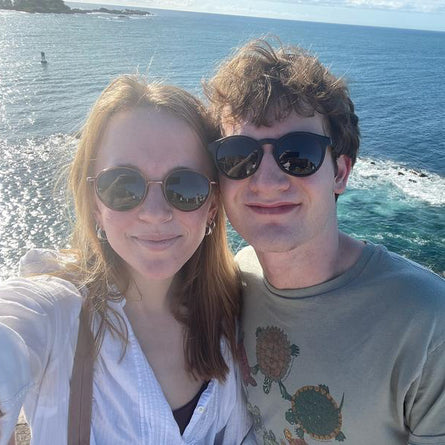Two people taking a selfie by the ocean with sunglasses on.