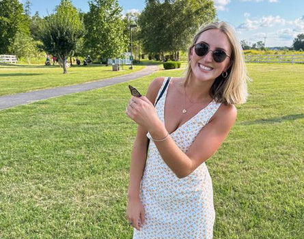 Woman in a white dress holding a phone in a park with green grass and trees.