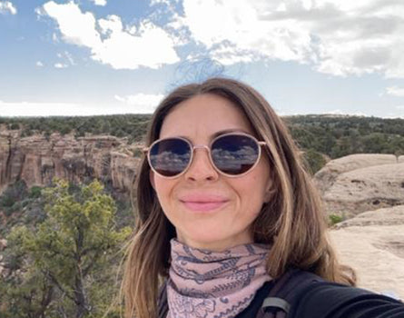 Woman wearing sunglasses with a scenic background of cliffs and trees