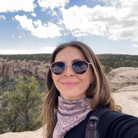 Woman wearing sunglasses with a scenic background of cliffs and trees