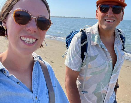 Two people on a beach with sunglasses and casual clothing