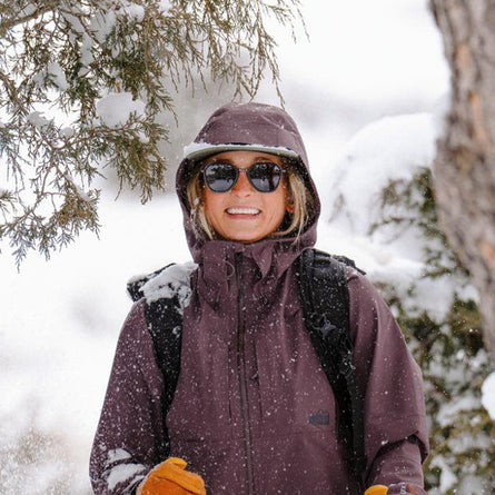 Person wearing a purple jacket and sunglasses in a snowy forest