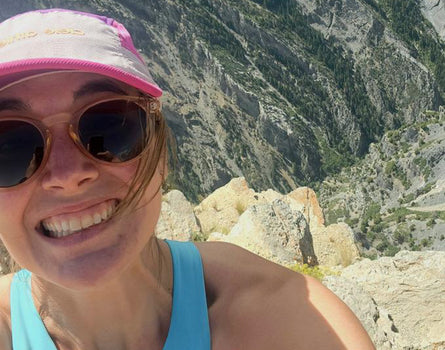 Person wearing sunglasses and a cap with a mountainous landscape in the background