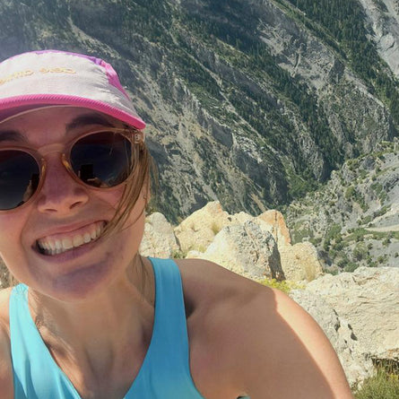 Person wearing sunglasses and a cap with a mountainous landscape in the background