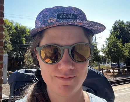 Person wearing a patterned cap and sunglasses outdoors on a sunny day.