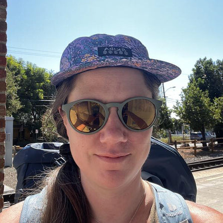 Person wearing a patterned cap and sunglasses outdoors on a sunny day.