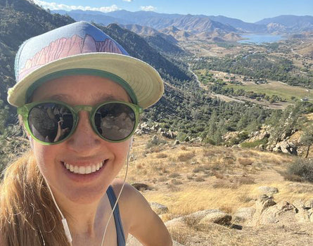 Person wearing sunglasses and a cap with a scenic mountain view in the background