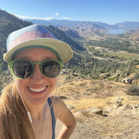 Person wearing sunglasses and a cap with a scenic mountain view in the background
