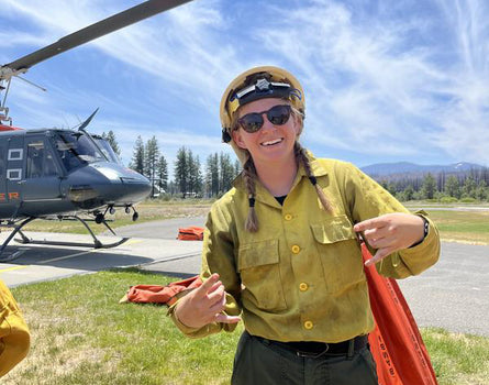 Person in a yellow firefighter uniform wearing sunglasses in front of a helicopter