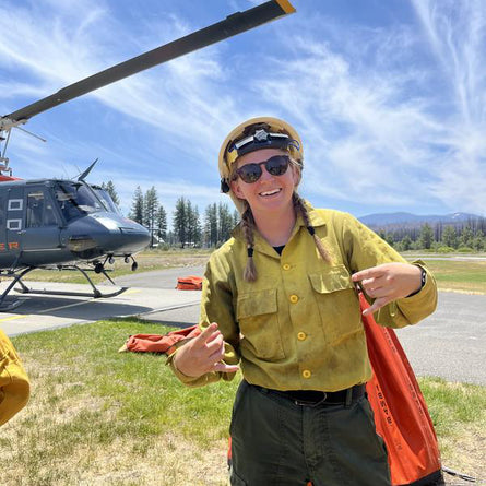 Person in a yellow firefighter uniform wearing sunglasses in front of a helicopter