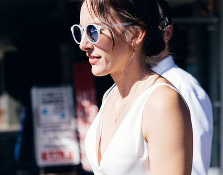 Woman wearing sunglasses and a white sleeveless top outdoors