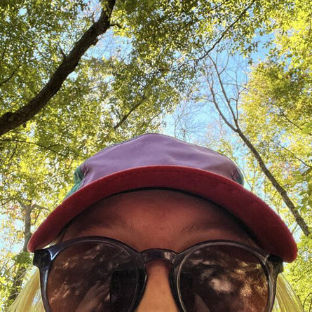 Person wearing a red cap and sunglasses with trees in the background