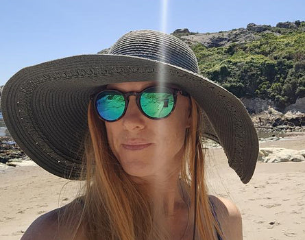 Person wearing a wide-brimmed hat and reflective sunglasses on a beach.