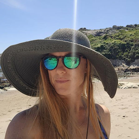 Person wearing a wide-brimmed hat and reflective sunglasses on a beach.