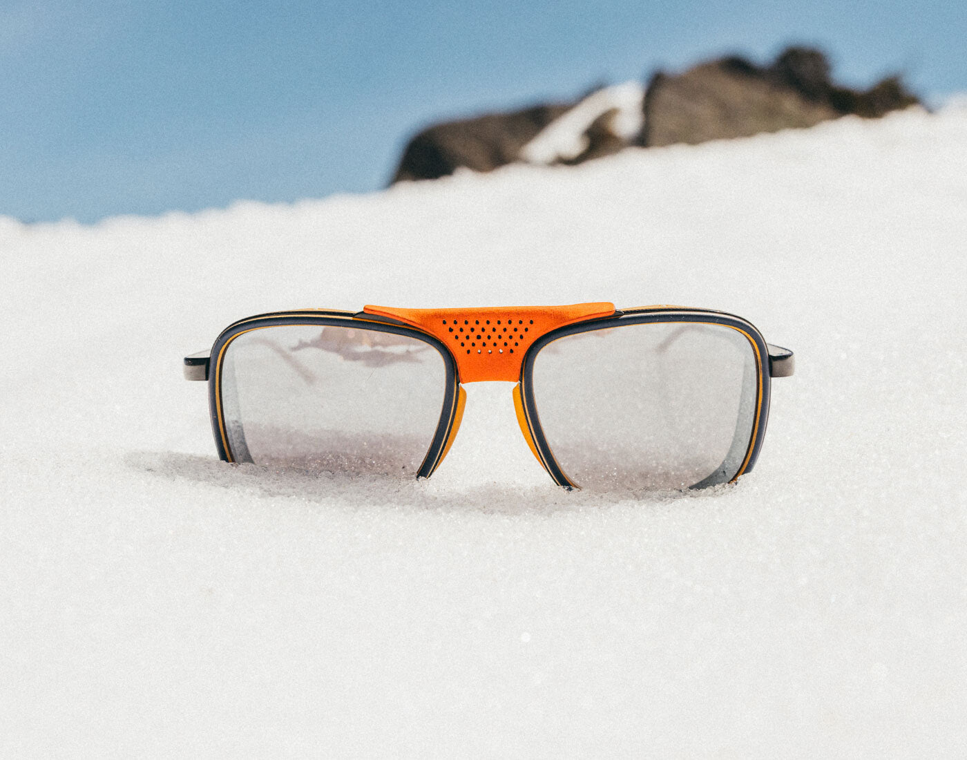 Sunglasses with orange frame and black lenses on a snowy surface