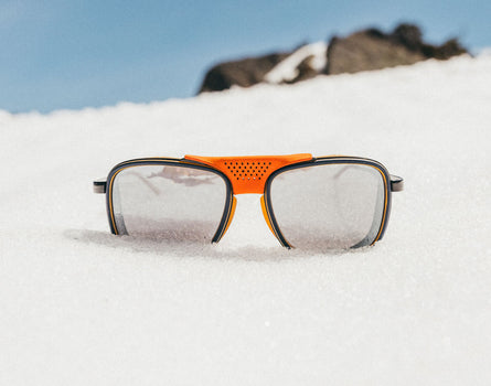 Sunglasses with orange frame and black lenses on a snowy surface