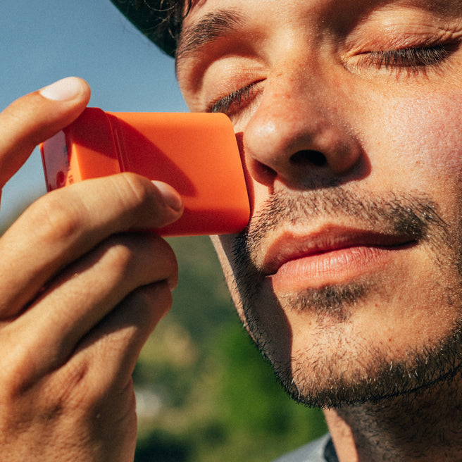 Man using an orange asthma inhaler with a blurred natural background