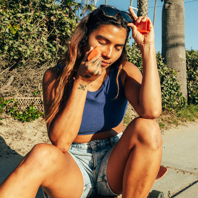 Woman applying sunscreen outdoors with palm trees in the background