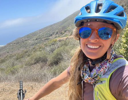 Person on a mountain bike wearing a helmet and sunglasses with a scenic background