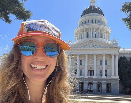 Person wearing sunglasses and a cap with the California State Capitol building in the background