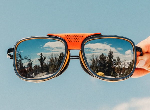 hand holding sunski ferrata sunglasses with reflection of trees in the lenses