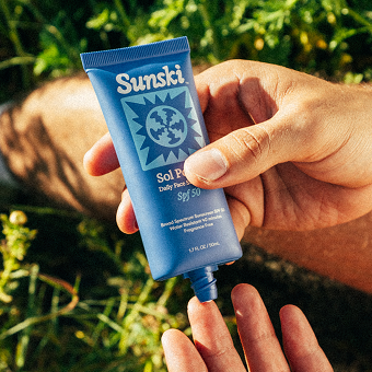 Hand holding a tube of Sunski sunscreen outdoors in the grass