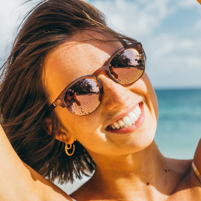 Woman wearing sunglasses with a beach and blue sky in the background
