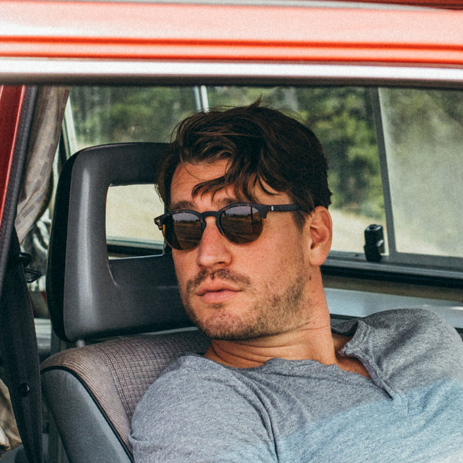 Man wearing sunglasses sitting inside a car with a blurred natural background