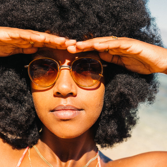 Woman wearing sunglasses with hands on head, blurred background