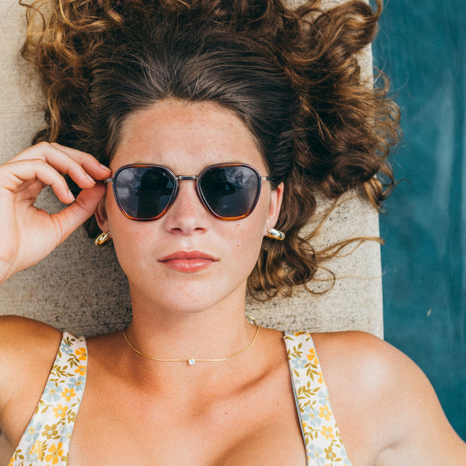 Bernina - Caramel Forest - Woman wearing sunglasses and a floral dress by a poolside