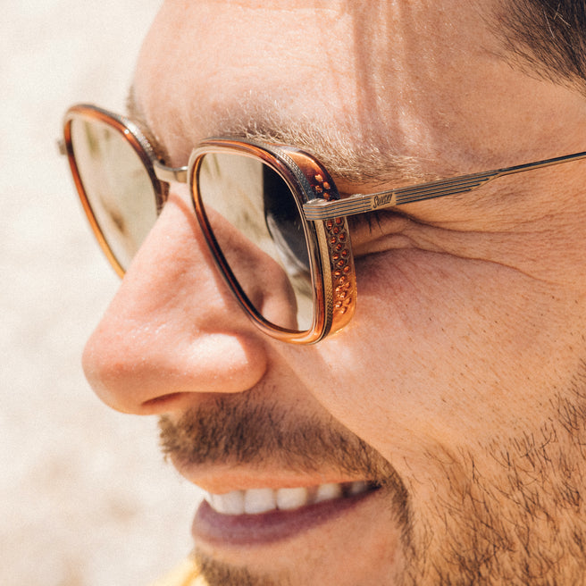 Bernina - Caramel Forest - Close-up of a person wearing gold-framed sunglasses with a blurred background