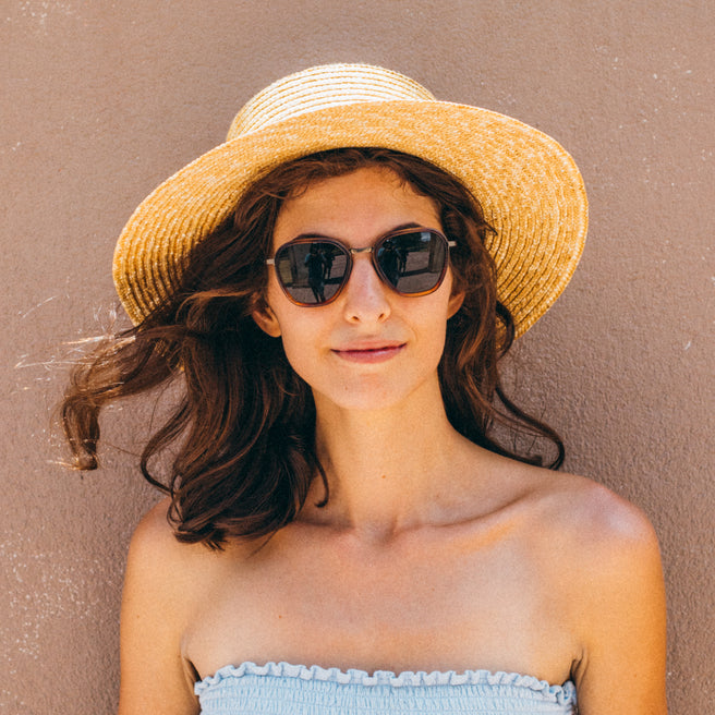 Bernina - Caramel Forest - Woman wearing a straw hat and sunglasses against a beige background
