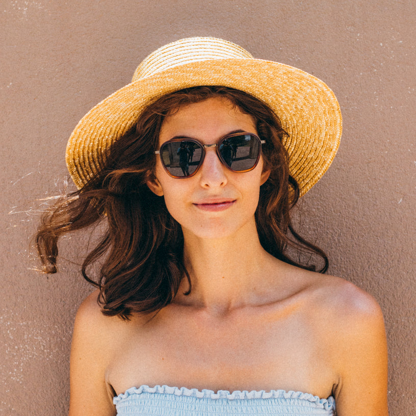 Woman wearing a straw hat and sunglasses against a beige background