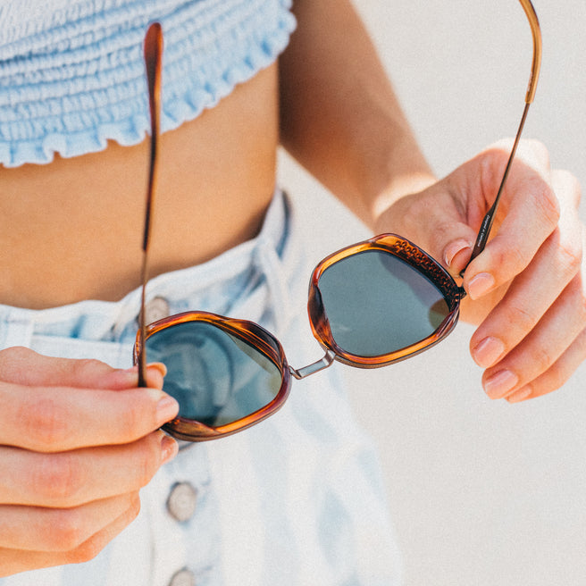Bernina - Caramel Forest - Person holding a pair of sunglasses with a blurred background