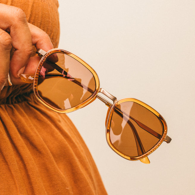 Bernina - Desert Amber - Person holding a pair of sunglasses with a neutral background