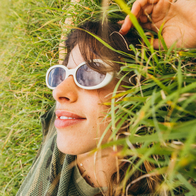 woman laying in grass with white sunglasses