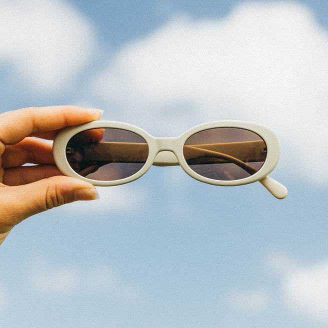 Hand holding sunglasses with a blue sky background
