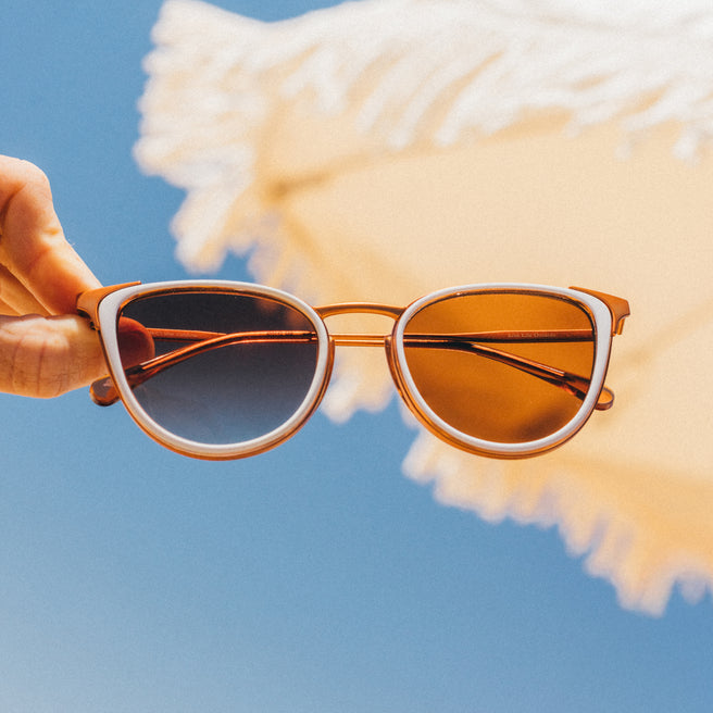Sunglasses held against a blue sky with a fluffy white cloud