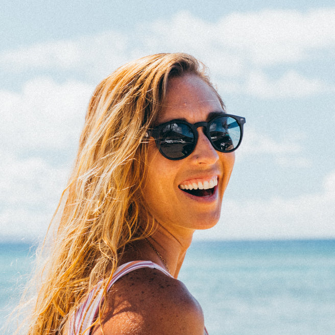 Woman wearing sunglasses with a beach and blue sky in the background