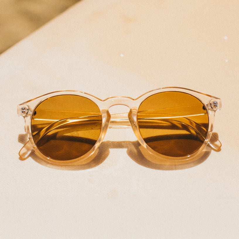 Round sunglasses with gold lenses on a beige surface