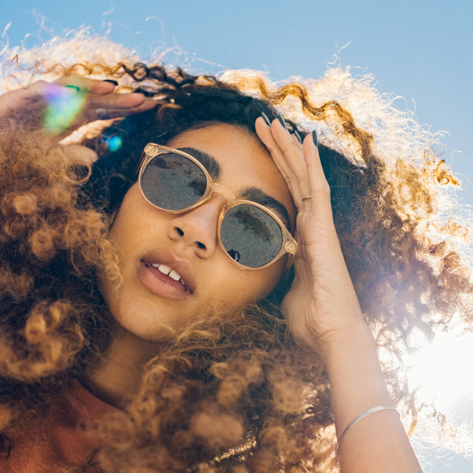 Woman with curly hair wearing sunglasses against a blue sky