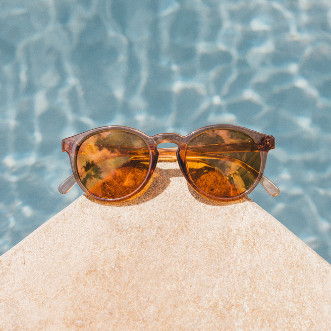 Brown sunglasses on a rock with a pool in the background